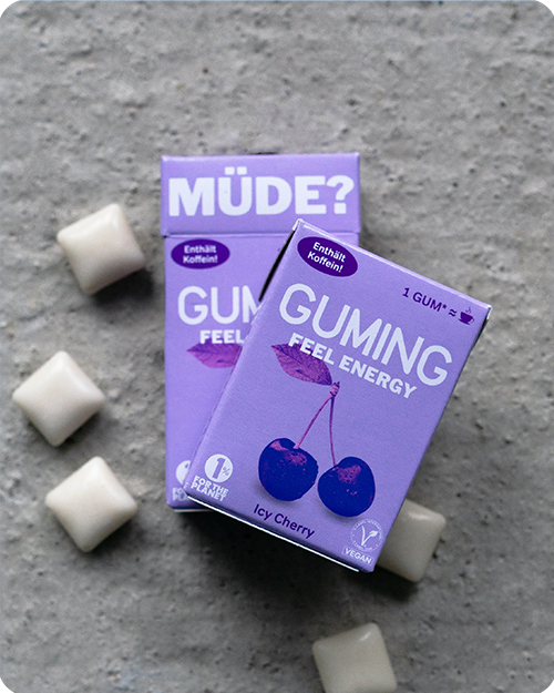 GUMING Energy Koffein Kaugummi mit Guarana und Vitaminen Verpackungen in Geschmacksrichtung Kirsche Icy Cherry auf Betonboden mit einzelnen Kaugummis