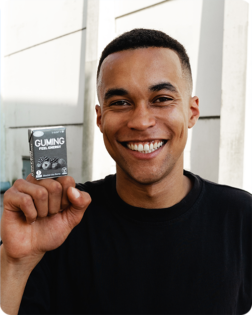 Model hält eine Packung GUMING Energy Koffein Kaugummi mit Koffein und Vitaminen in Geschmacksrichtung Blacker The Berry auf seiner geschlossenen Faust